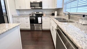 A modern kitchen with white cabinets, stainless steel appliances, granite countertops, and a large window with blinds.