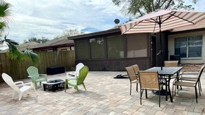 An outdoor patio with stone flooring, green and white chairs, a table, and a striped umbrella.