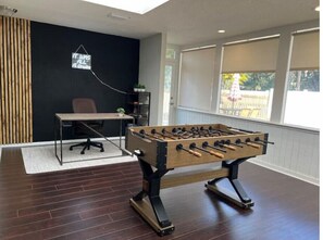 A room with a foosball table, a desk, and a chair.