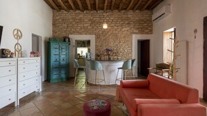 A cozy living room with a stone wall, a red sofa, a bar area with stools, and a white cabinet with drawers. - Boho-chic Villa in San Rafael 1min (Sant Antoni de Portmany)
