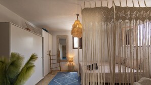 A bedroom with a bed, a hanging light fixture, a mirror, and a blue patterned rug. - Boho-chic Villa in San Rafael 1min (Sant Antoni de Portmany)