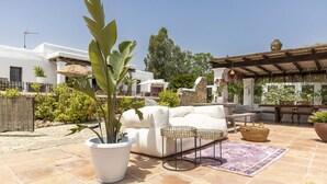 An outdoor patio area with a white sofa, a large potted plant, wicker tables, and a stone floor. - Boho-chic Villa in San Rafael 1min (Sant Antoni de Portmany)
