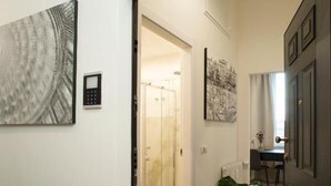 Een hal met een glazen douchedeur, een potplant en kunstwerken aan de muur.