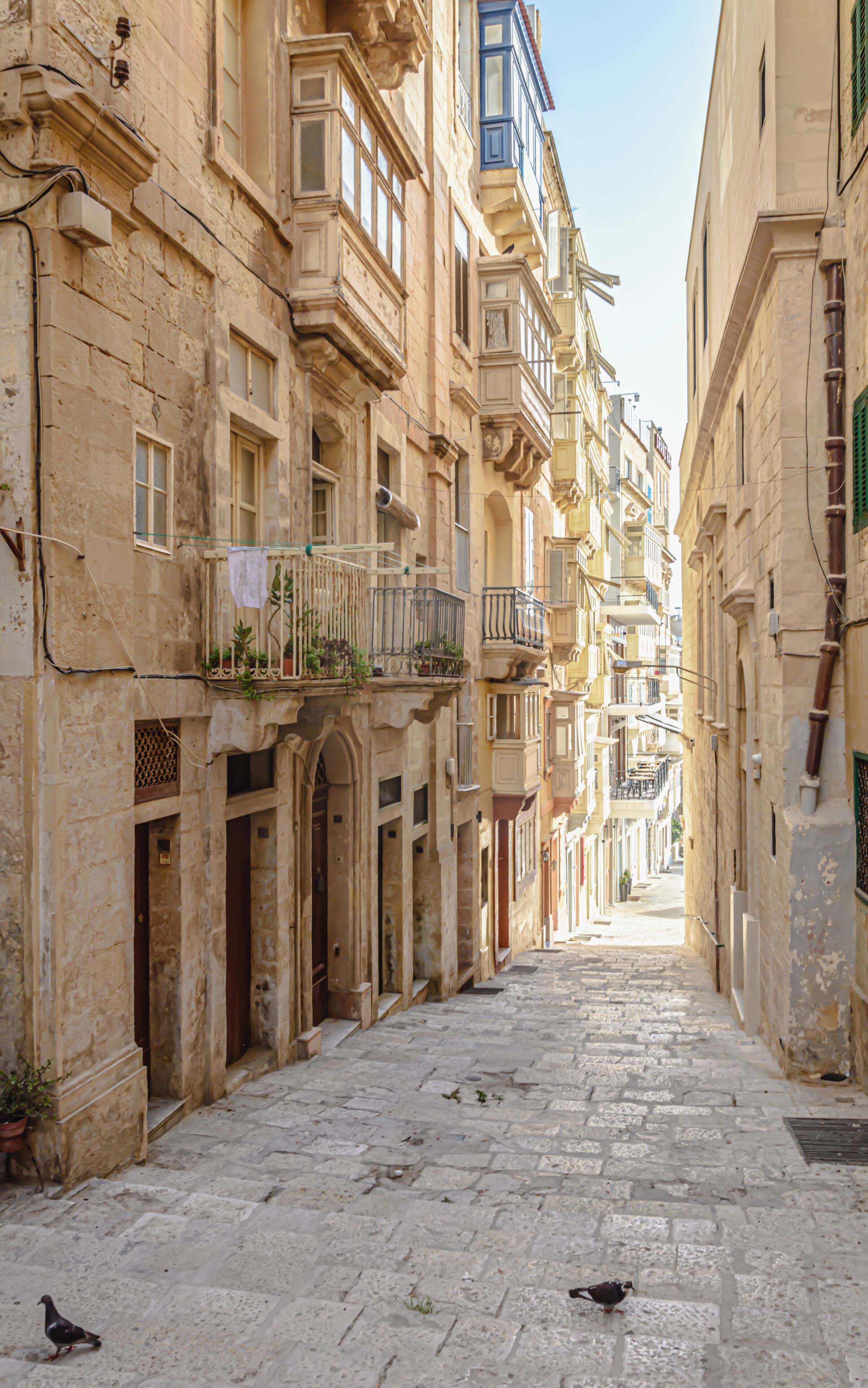 Une ruelle étroite pavée, bordée de bâtiments historiques dotés de balcons et de portes en arc de cercle.