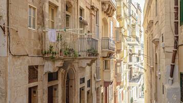 Une ruelle étroite pavée, bordée de bâtiments historiques dotés de balcons et de portes en arc de cercle.