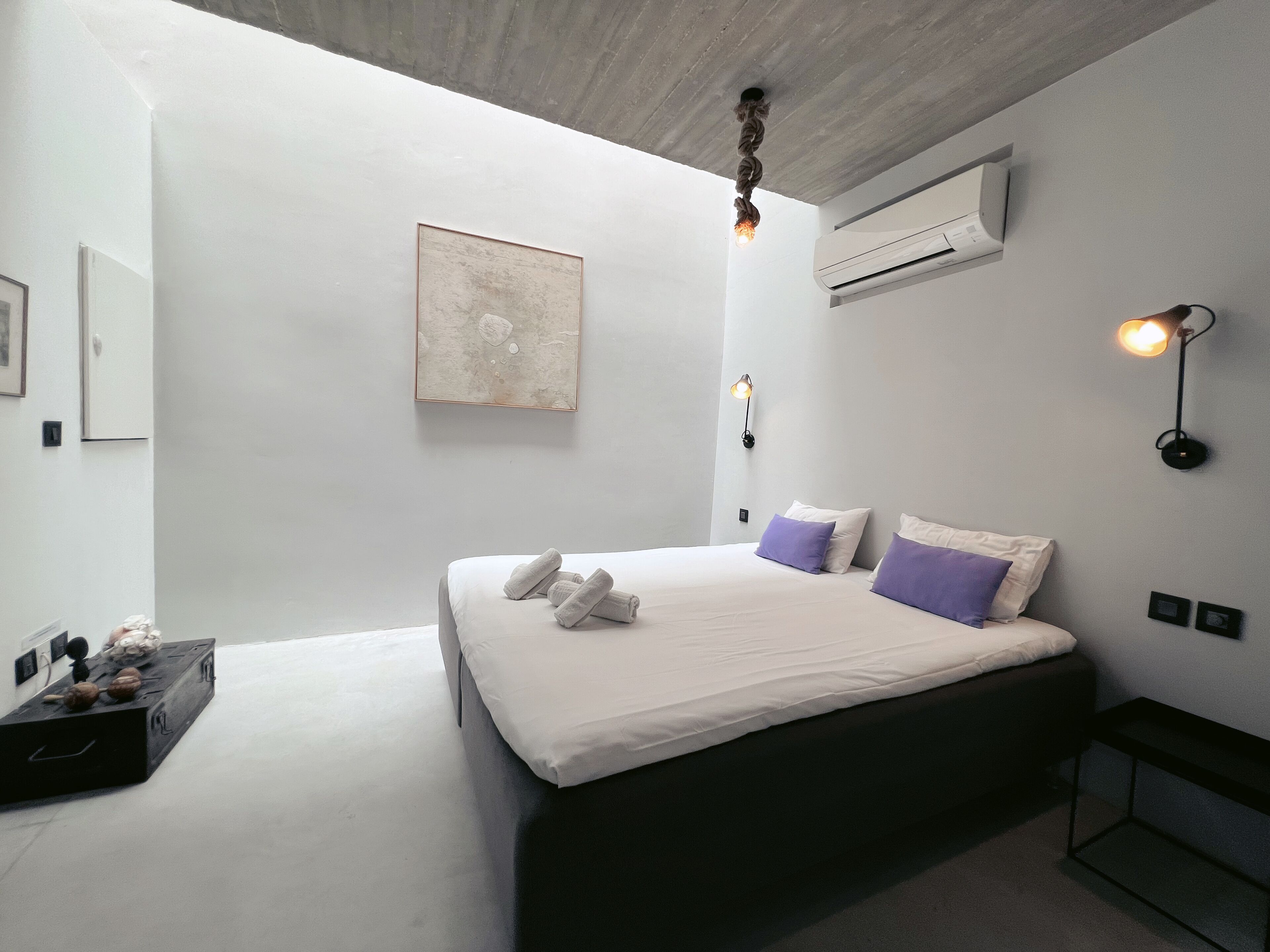 Een moderne slaapkamer met een groot bed, een wandairconditioner, een ingelijst kunstwerk en een bedlampje.