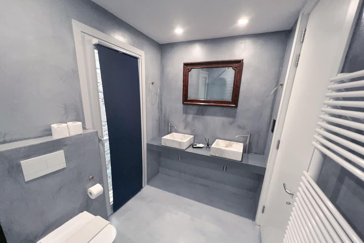 A bathroom with a toilet, two sinks, a mirror, and a towel rack.
