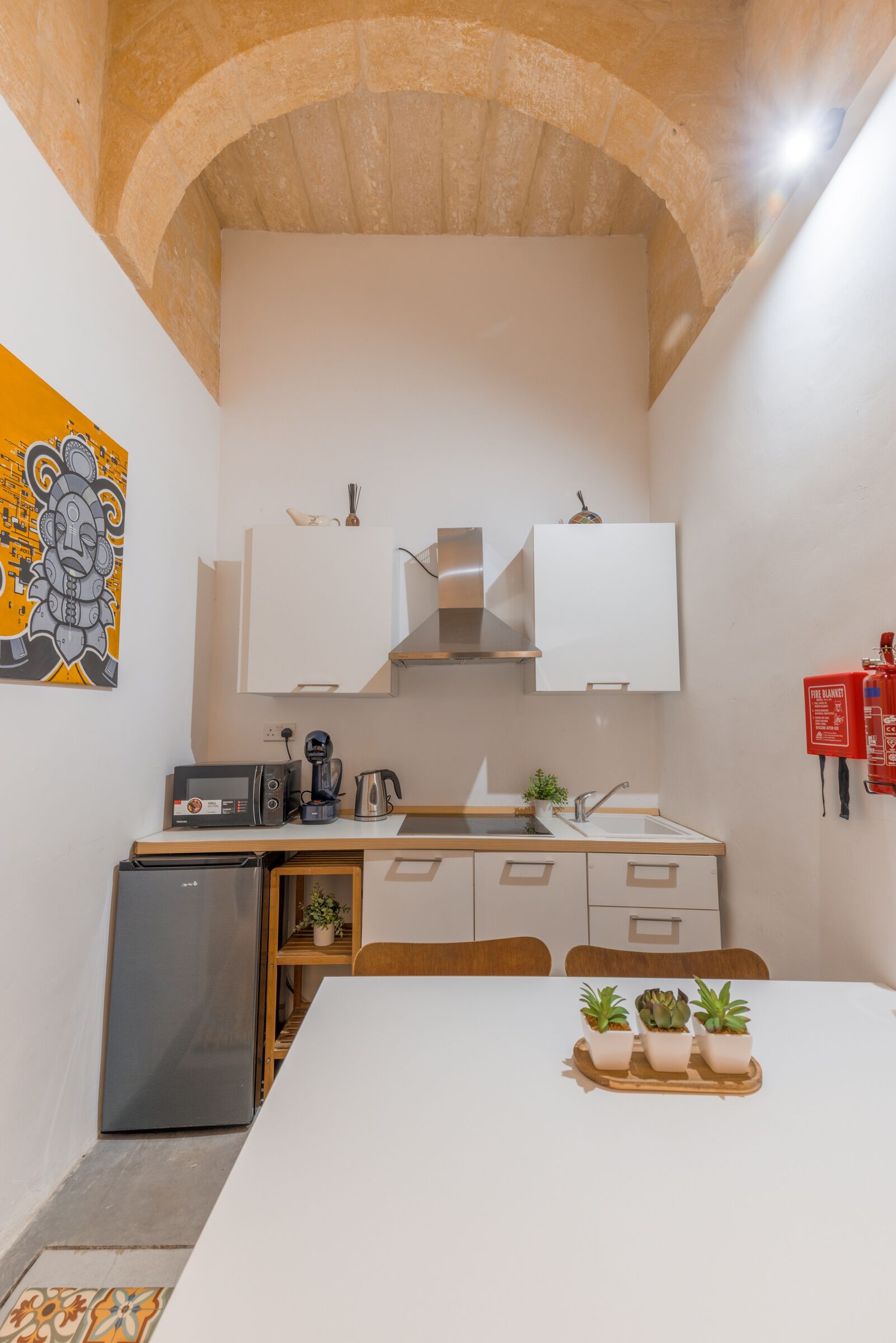 Eine kompakte Küche mit weißen Schränken, einer Mikrowelle, einer Kaffeemaschine und einem kleinen Kühlschrank.