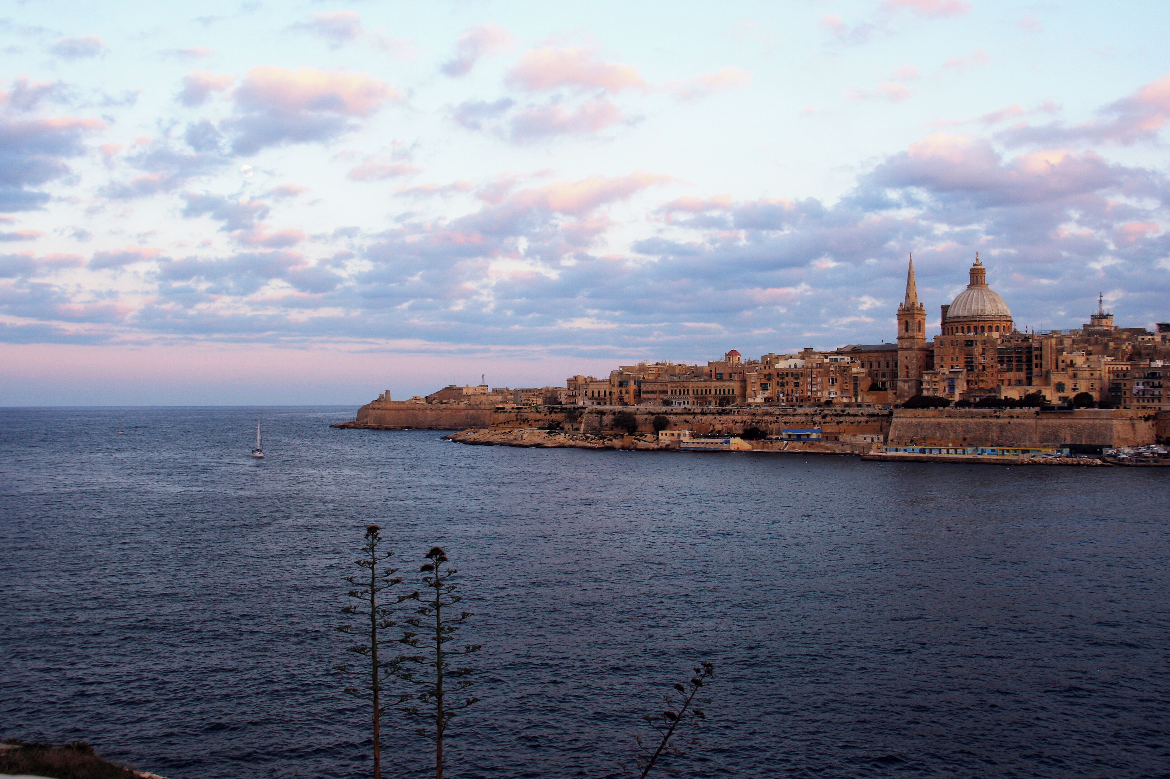 Un paysage urbain côtier caractérisé par une architecture historique, un dôme imposant et un port fortifié.