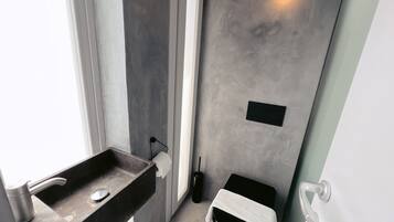 A bathroom with a dark sink, a towel rack, a small black trash bin, and a light fixture on the wall.