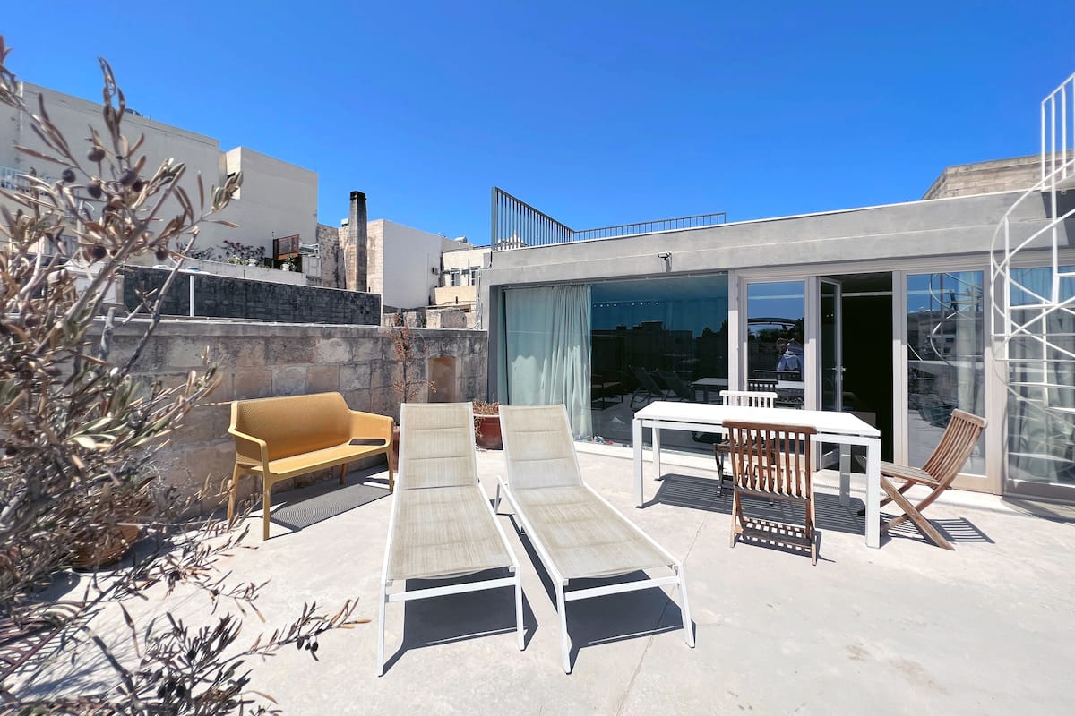 A rooftop terrace with a seating area, including a sofa and lounge chairs, and a table.