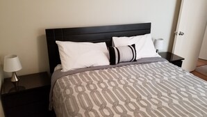 Un lit bien fait, avec une couvre-lit à motifs, deux oreillers et une tête de lit sombre.
