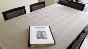 Une brochure est posée sur une table recouverte d’une nappe à motifs géométriques, et quatre chaises l’entourent.
