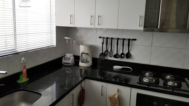 Une cuisine moderne avec des meubles blancs, un plan de travail noir, une machine à café et divers ustensiles accrochés au mur.