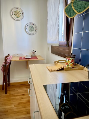 Uma cozinha com mesa de madeira, uma cadeira, uma janela com cortinas e duas placas decorativas na parede.