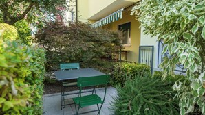 A small outdoor seating area with a table and chairs, surrounded by greenery and a building with a yellow facade. - Cosy studio with garden and free parking, close to Airport and Venice (Venezia)