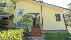 A yellow building with a tiled entrance, a green awning, and a small tree in the foreground. - Cosy studio with garden and free parking, close to Airport and Venice (Venezia)