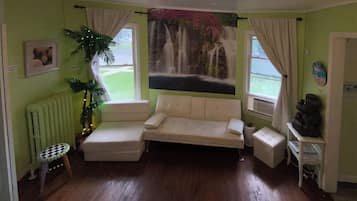 Ein Zimmer mit einer Couch, einem kleinen Tisch, einem Heizkörper, einer Pflanze und einem Gemälde eines Wasserfalls.
