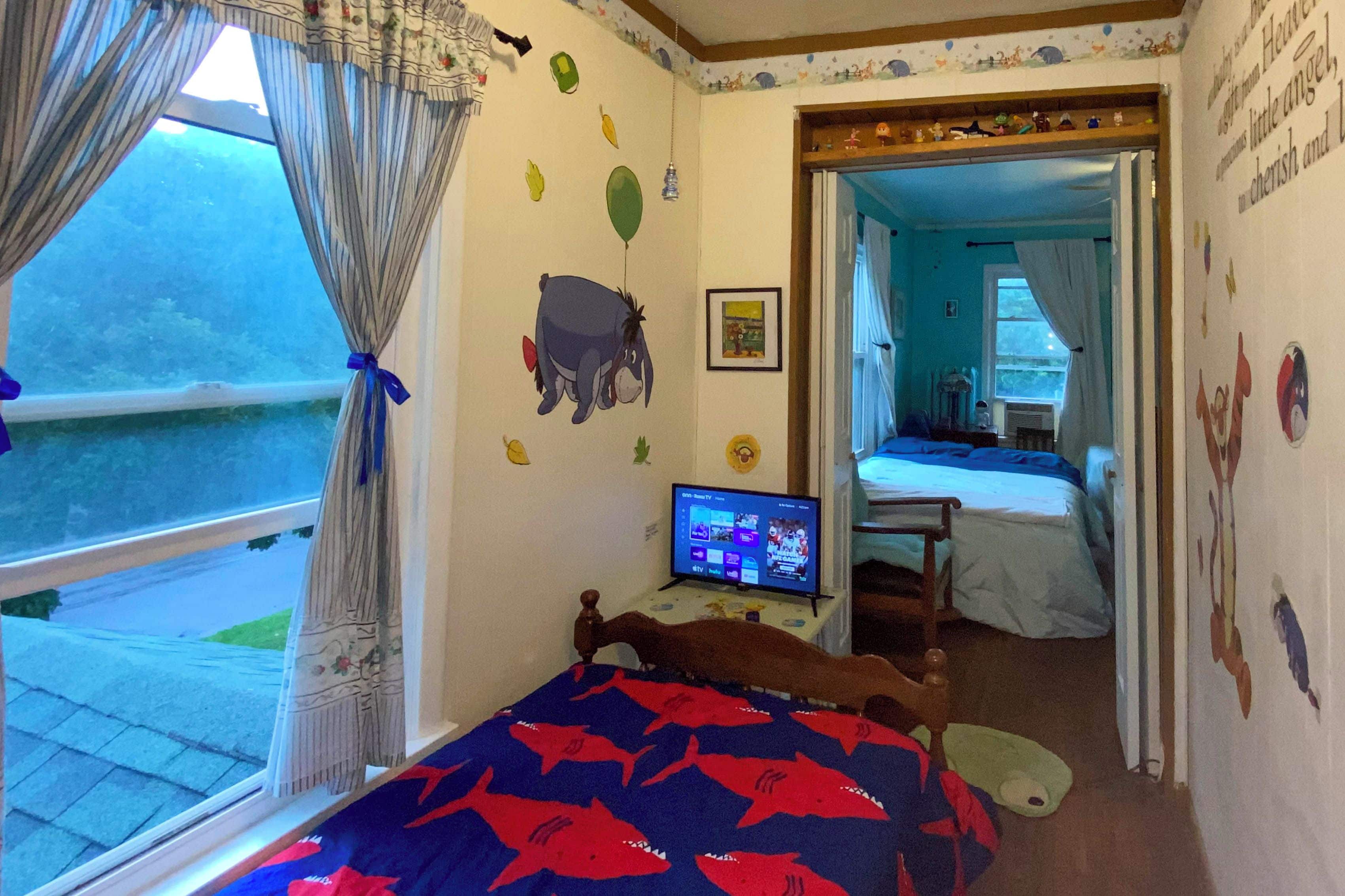 A bedroom with a bed, a television, and a window with curtains.