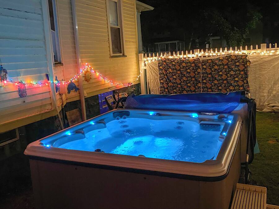 Ein Whirlpool mit blauem Licht, umgeben von einem weißen Zaun und Lichterketten.