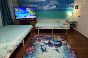 A hotel room with two beds, a TV, a nightstand, and a mural of a beach scene.