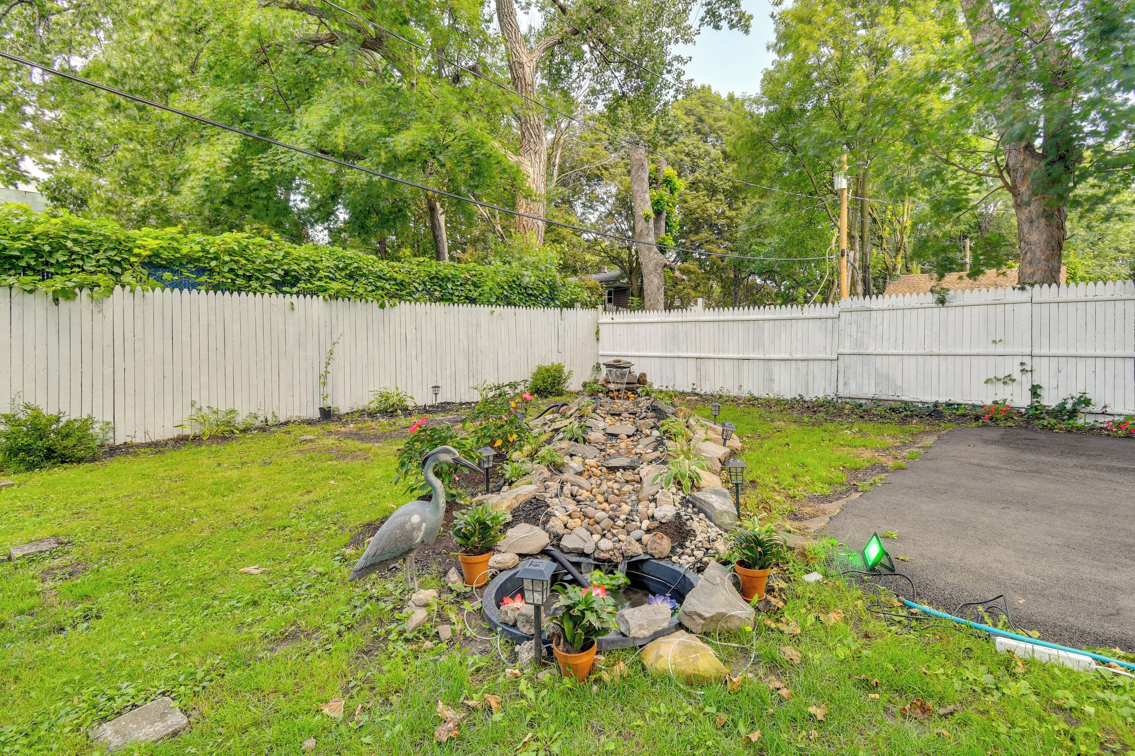 A garden with a water feature, potted plants, and a white picket fence.