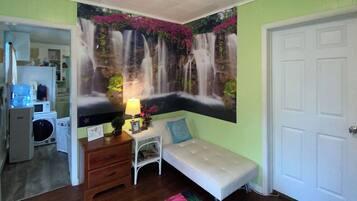 Una habitación con un mural de cascada, un banco blanco, una mesita con lámpara y una puerta.
