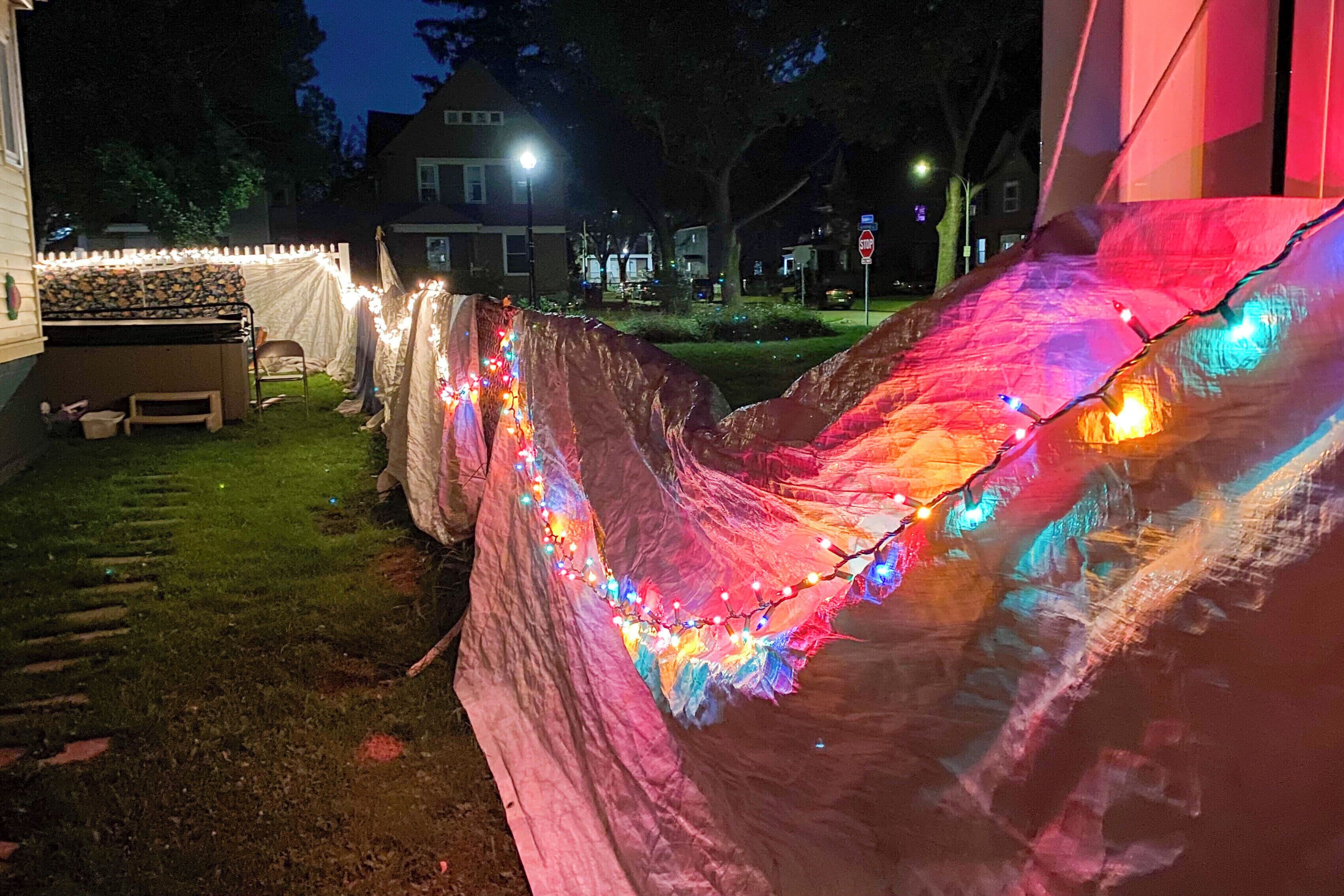Una carpa con luces de colores y una valla de piquetes blancos en un patio trasero.