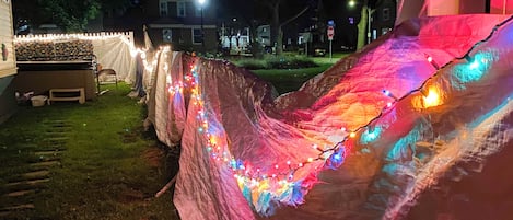 Una carpa con luces de colores y una valla de piquetes blancos en un patio trasero.