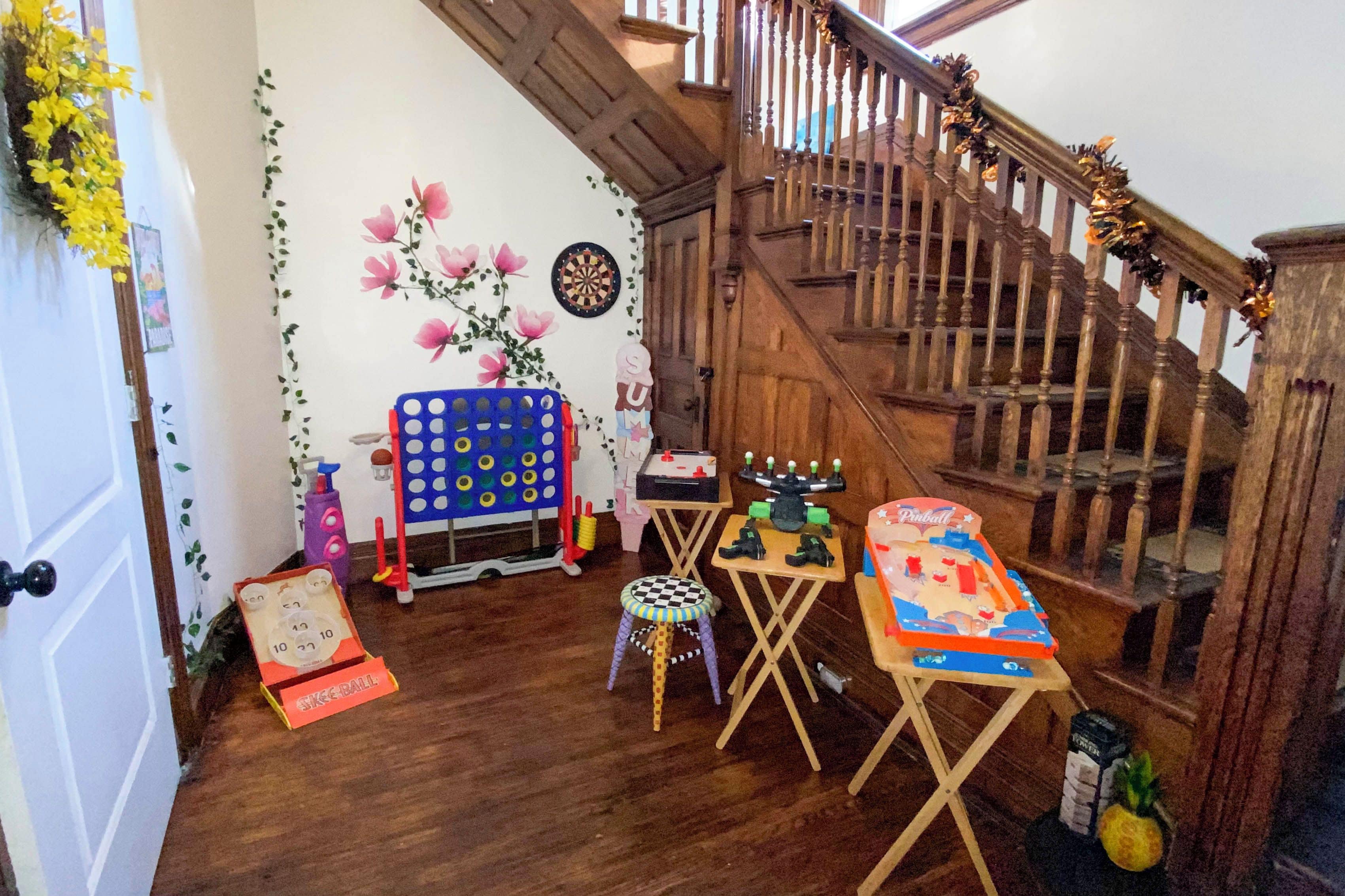 Una habitación con una escalera de madera, un dardo, un juego de mesa azul, una pequeña mesa con una silla y un coche de juguete.