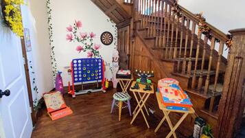 Una habitación con una escalera de madera, un dardo, un juego de mesa azul, una pequeña mesa con una silla y un coche de juguete.