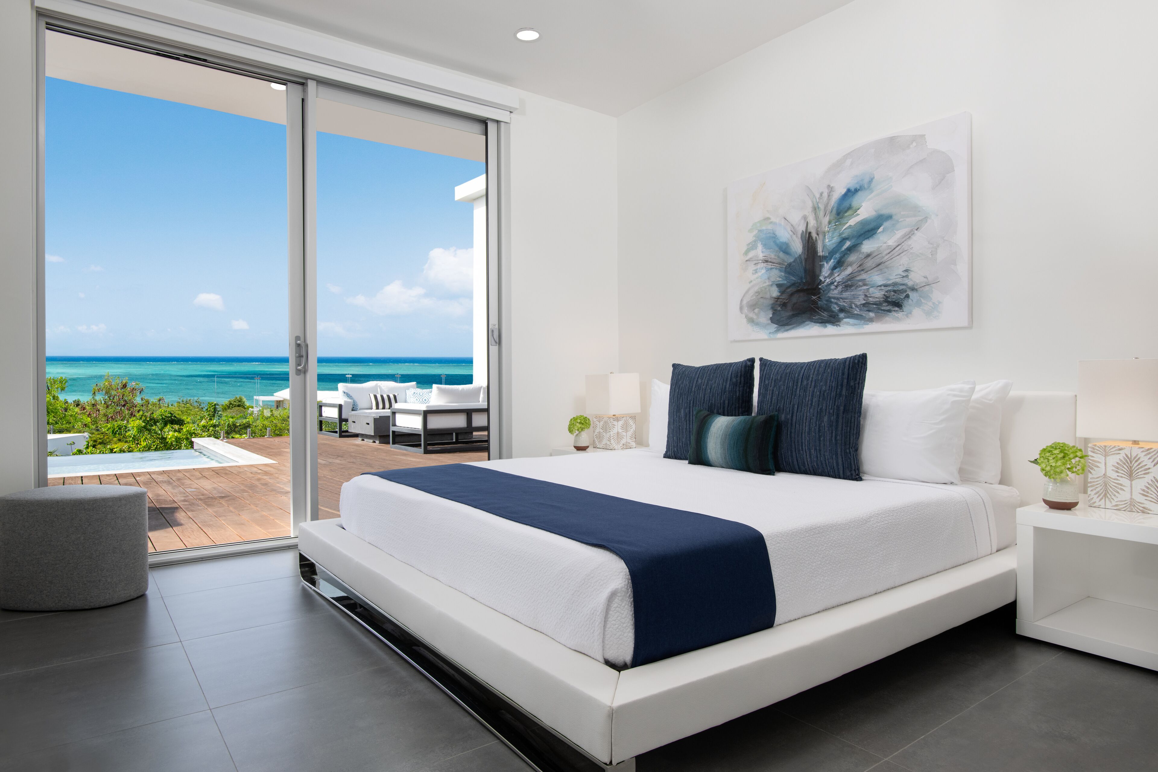 Un dormitorio moderno con una cama grande, un ventanal corredero que da a un balcón con vistas al océano.