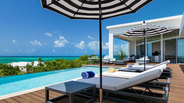 A poolside area with lounge chairs, umbrellas, and a view of the ocean. - Mistral, Ocean view 3BR villa 7 min from beach (Providenciales)