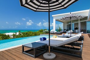Un espace aménagé au bord de la piscine, avec des chaises longues, des parasols et une vue sur l’océan.