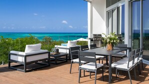 A modern outdoor patio with a view of the ocean, a dining table with chairs, and a grill. - Mistral, Ocean view 3BR villa 7 min from beach (Providenciales)