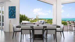 A modern dining area with a large table and chairs, a vase, and a view of the ocean and greenery. - Mistral, Ocean view 3BR villa 7 min from beach (Providenciales)