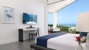 A modern hotel room with a large bed, a desk, and a view of the ocean. - Mistral, Ocean view 3BR villa 7 min from beach (Providenciales)