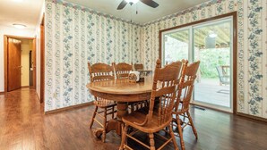 Une salle à manger avec une table et des chaises en bois, un ventilateur de plafond et un papier peint à motifs floraux.
