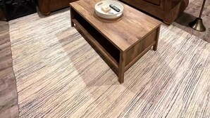Una sala de estar con un sofá seccional marrón, una mesa de centro de madera y un espejo grande en la pared.