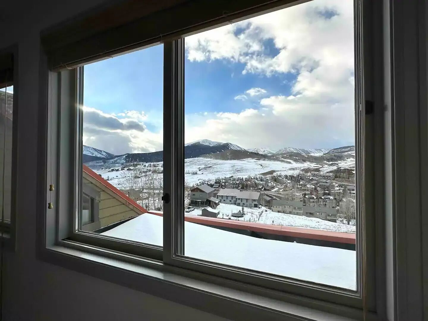 Huone, jossa on suuri ikkuna, josta avautuu näkymä lumiseen maisemaan, jossa on vuoria ja alapuolella sijaitseva kaupunki.