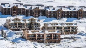Un resort cubierto de nieve con varios edificios de varios pisos, que incluyen balcones y grandes ventanales.