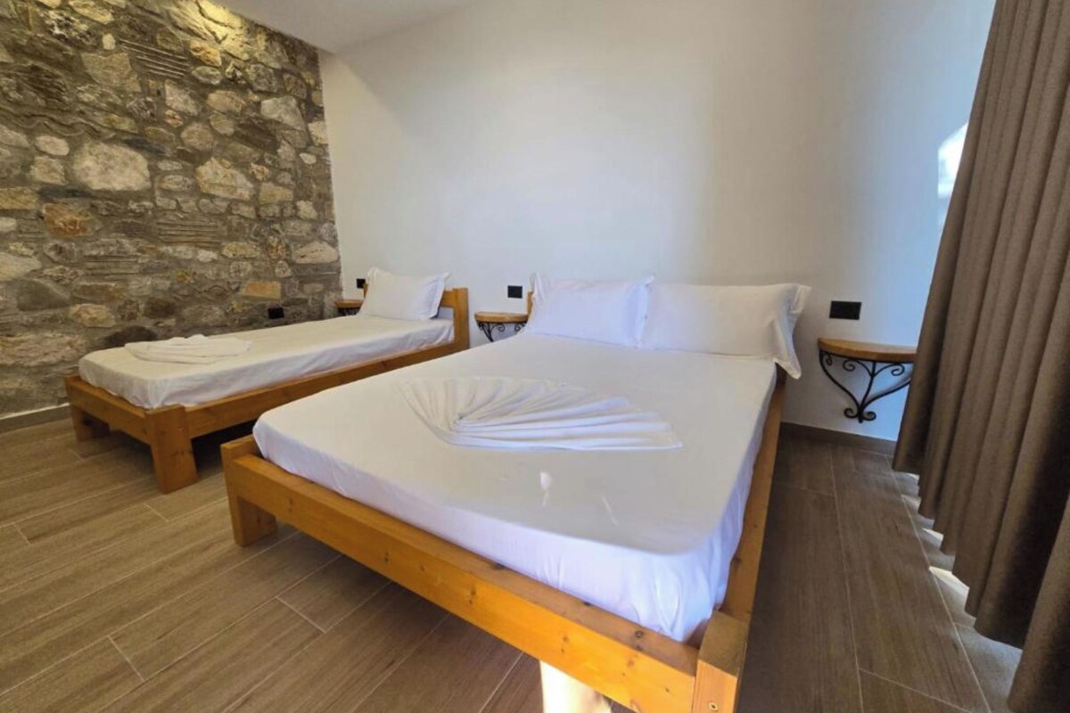 A room with two wooden beds, white linens, a stone wall, and a wooden floor.