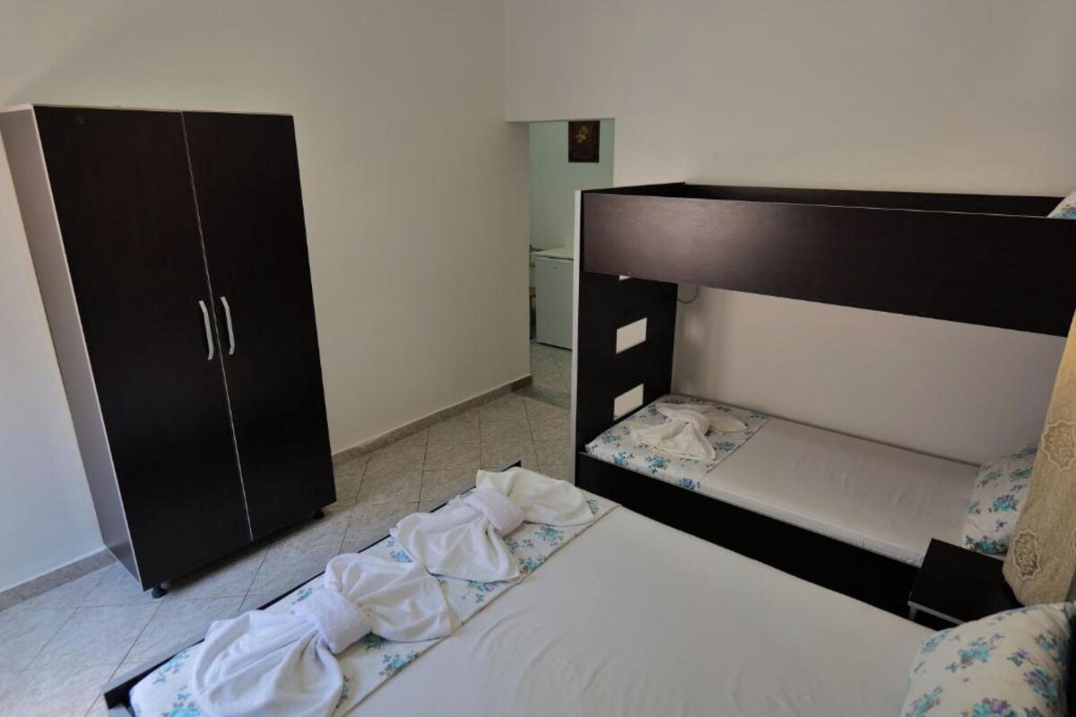 Un dormitorio con una cama litera, un armario y un baño al fondo.