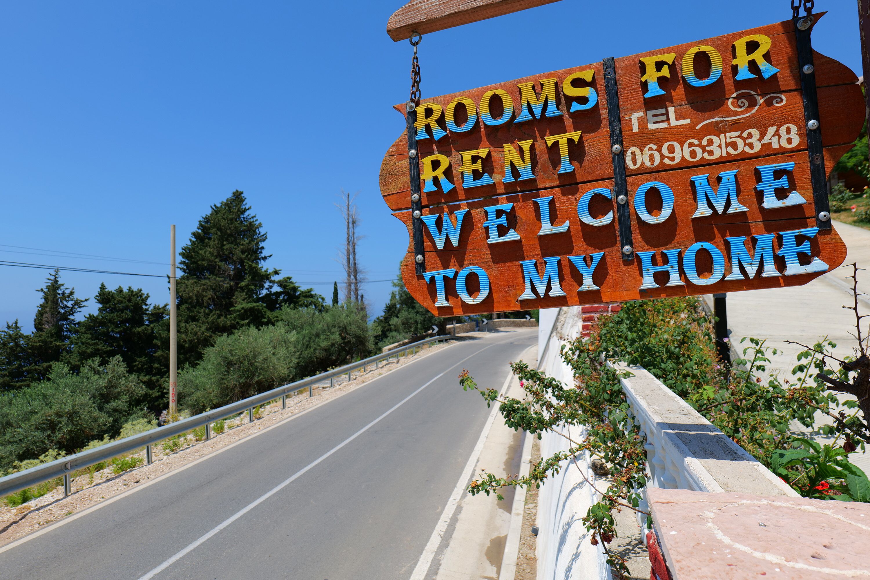 A wooden sign with the text "ROOMS FOR RENT WELCOME TO MY HOME" and a phone number.