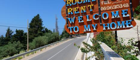 A wooden sign with the text "ROOMS FOR RENT WELCOME TO MY HOME" and a phone number.