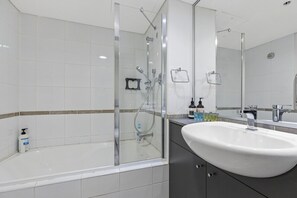 Enjoy a refreshing shower in the bathroom, featuring a large sink, glass-enclosed shower with handheld showerhead, and ample storage for toiletries.