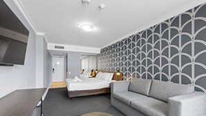 Habitación de hotel con cama, sofá, escritorio y una mesa de centro redonda.