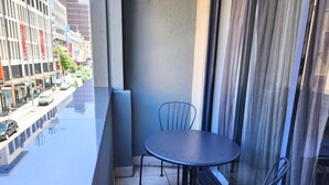 Un balcón con una mesa y sillas, vista a la calle y fachada de un edificio.