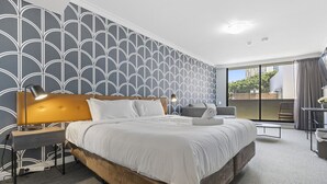 Habitación de hotel con una cama grande, dos mesitas de noche con lámparas, un escritorio pequeño y vistas al exterior.
