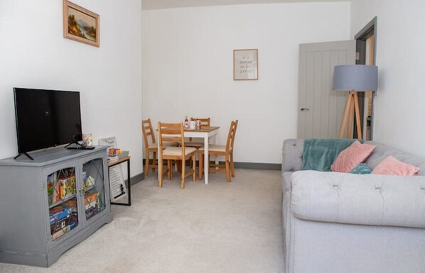 A living room with a grey sofa, a TV on a cabinet, a dining table with chairs, and a lamp. - The Perfect Retreat: The Luxury Dartmoor Den, Ashburton, Dartmoor, Devon (Ashburton, Newton Abbot)